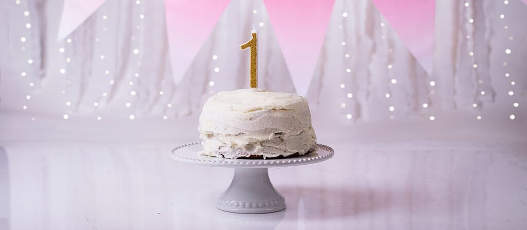 Gâteau d'anniversaire blanc sur un promontoire placé sur un sol blanc réfléchissant et avec une banderole rose en fond