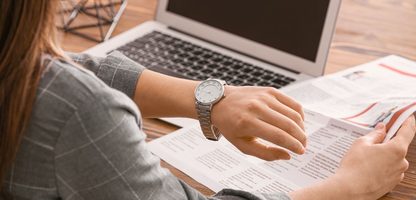 femme devant son ordinateur qui regarde sa montre pour calculer les pénalités de retard de paiement de sa facture